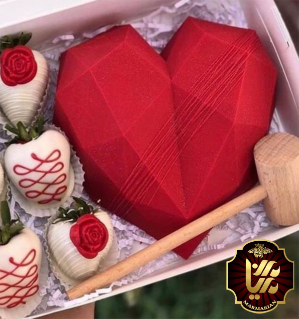 یک قلب قرمز بزرگ و شکلات های خامه ای قلبی درون یک جعبه و یک چکش چوبی در کنار آن ها
