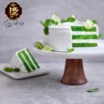 یک کیک بزرگ خامه ای سفید و سبز بر روی یک پایه و یک تکه کیک بر روی یک ظرف